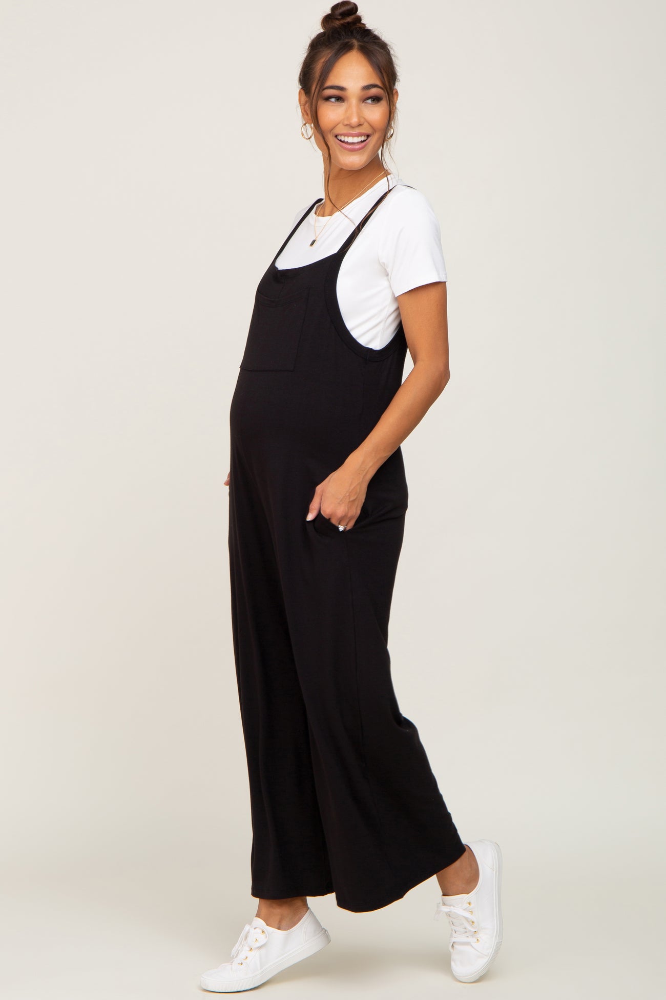 woman wearing a black maternity jumpsuit over a white t-shirt and smiling, showcasing her baby bump