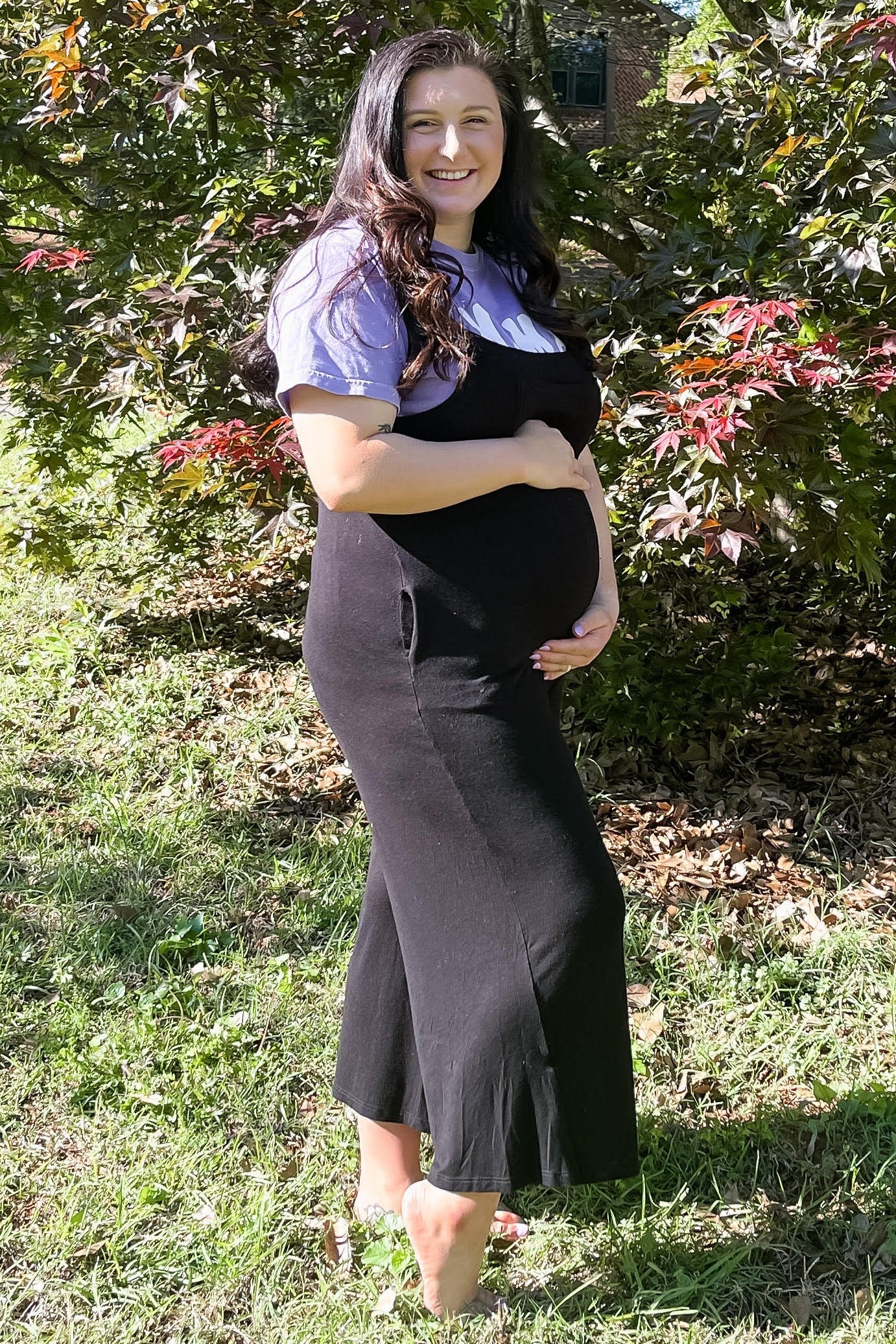 woman wearing a black maternity dress with a white top, showing her baby bump while standing outdoors