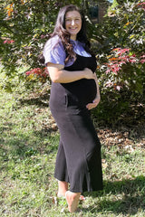woman wearing a black maternity dress with a white top, showing her baby bump while standing outdoors