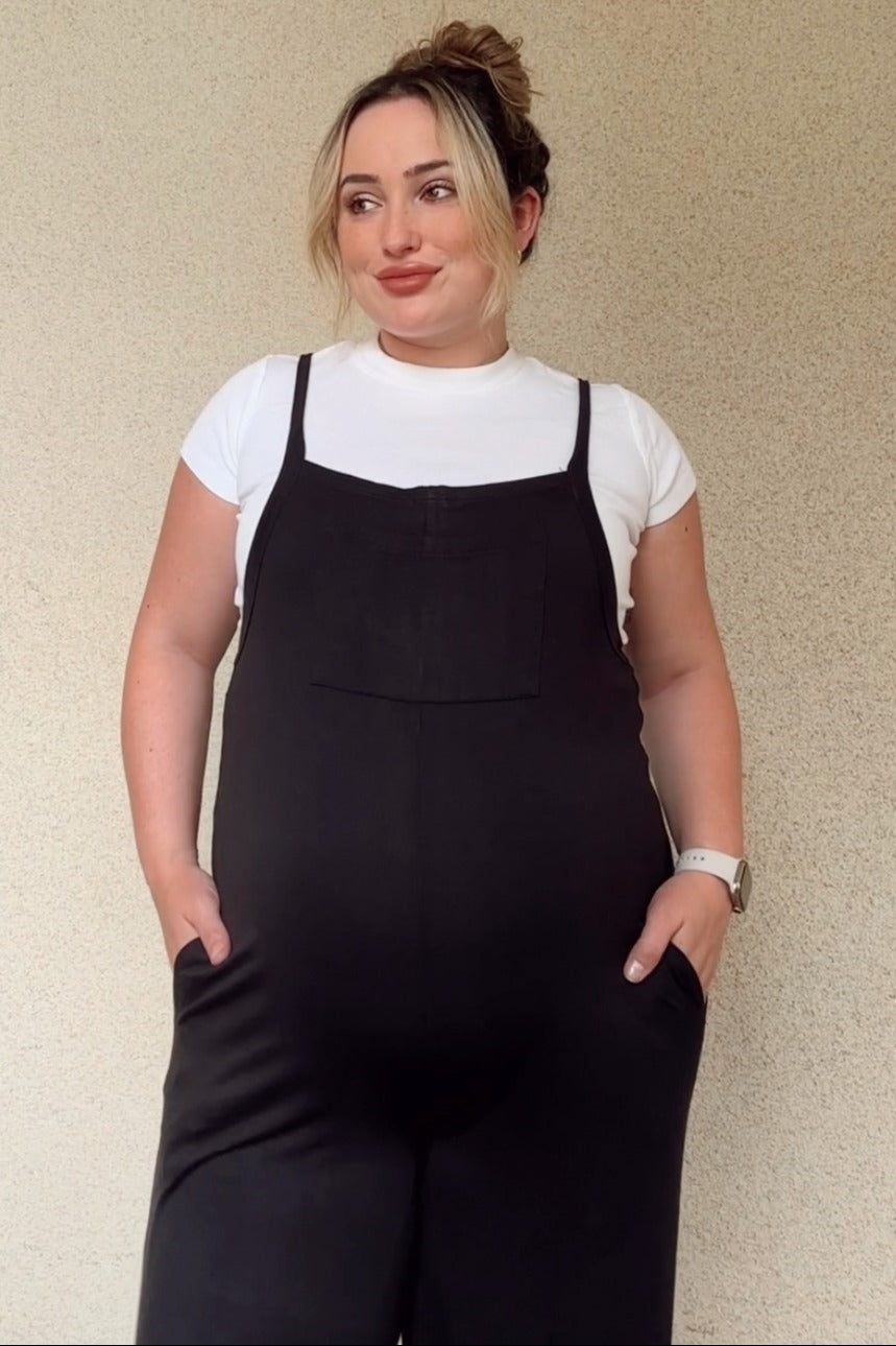 woman wearing a black maternity jumpsuit over a white t-shirt with pockets, showcasing her baby bump