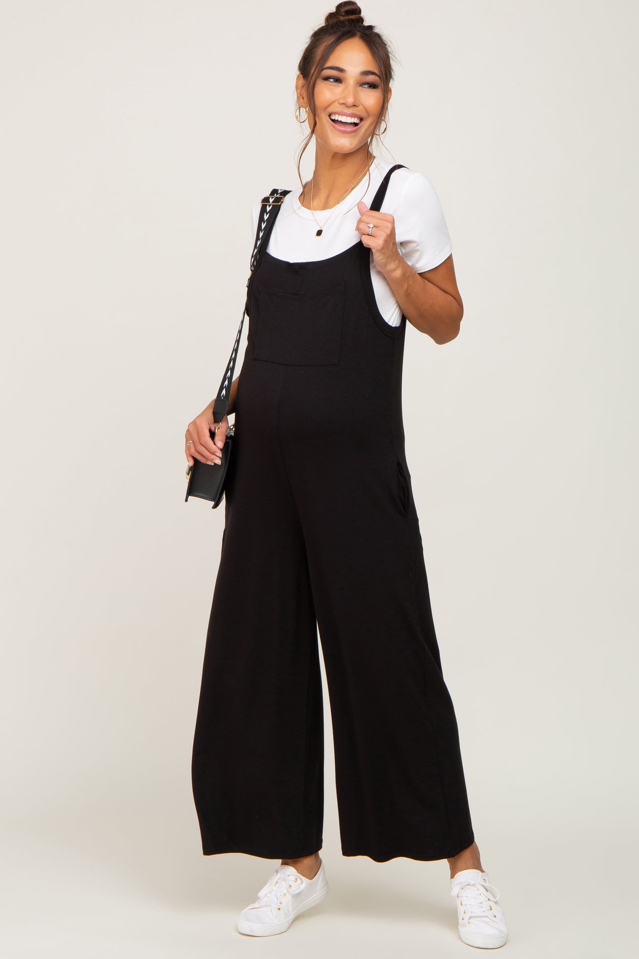 woman wearing a black maternity jumpsuit over a white short sleeve top with a baby bump visible and smiling