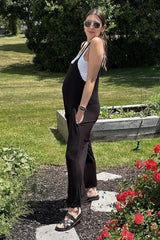 woman wearing a black maternity jumpsuit, showing her baby bump, standing outdoors near garden flowers.
