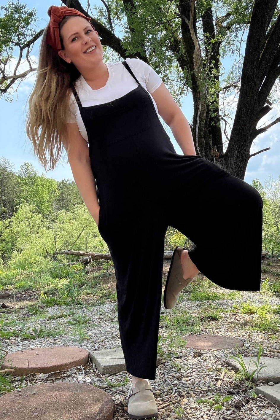 woman wearing a black maternity jumpsuit with a white t-shirt underneath and a headband, showing her baby bump