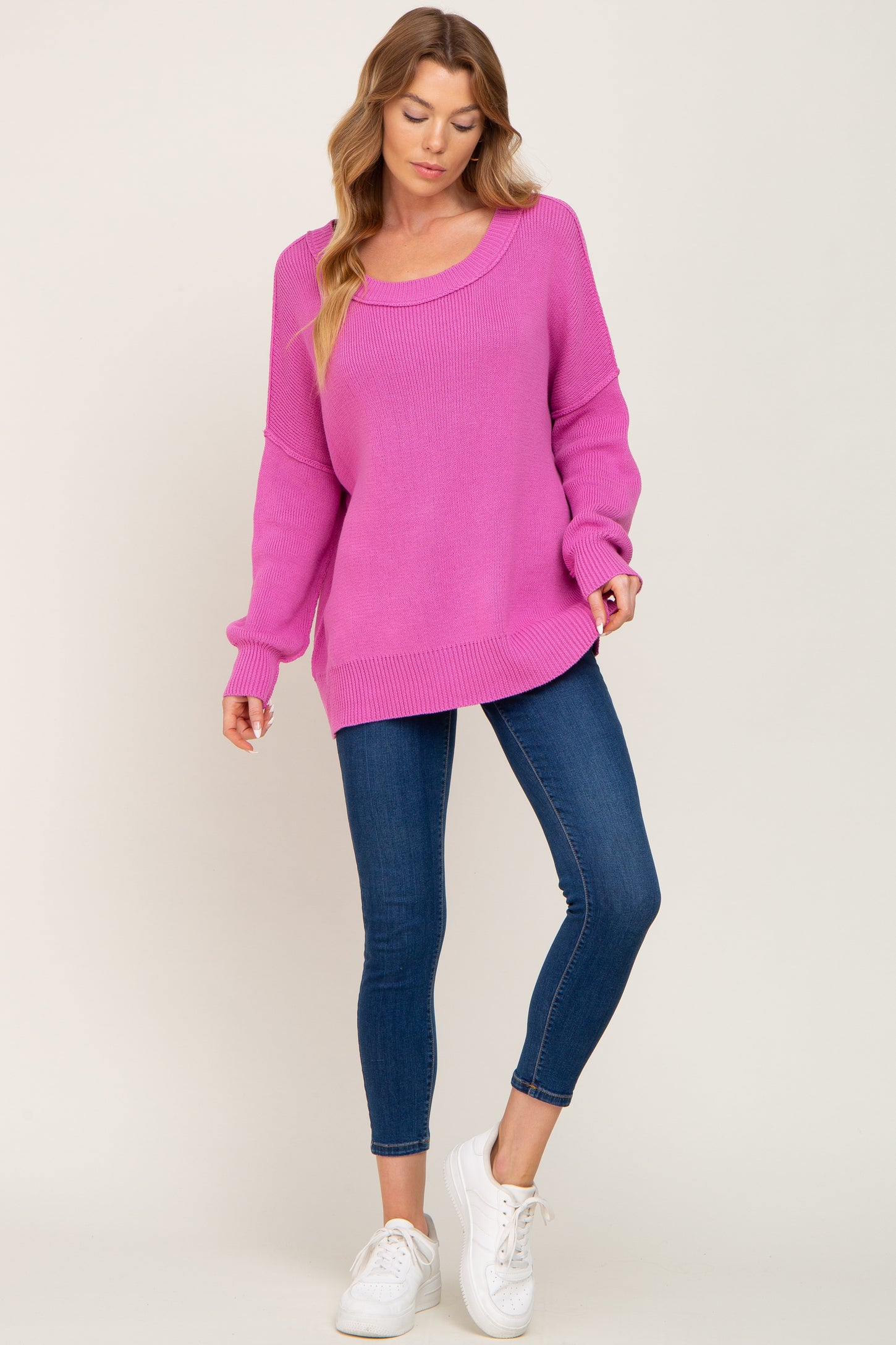 woman wearing a bright pink oversized sweater with a scoop neckline and blue skinny jeans, paired with white sneakers