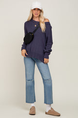 woman wearing a dark purple off-the-shoulder sweater, light blue cropped jeans, and a white cap with a black crossbody bag