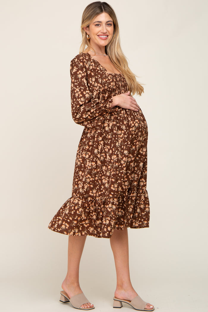 Pregnant woman in a brown floral long sleeve maternity midi dress with smocked bodice and ruffled hem