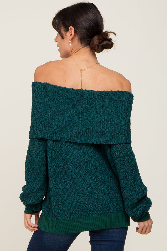 Woman wearing a dark green off-the-shoulder knit sweater with a fold-over neckline and long sleeves