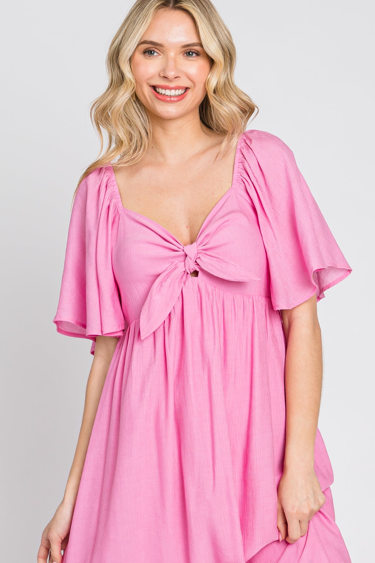 woman wearing a pink tie-front dress with flutter sleeves and a relaxed fit