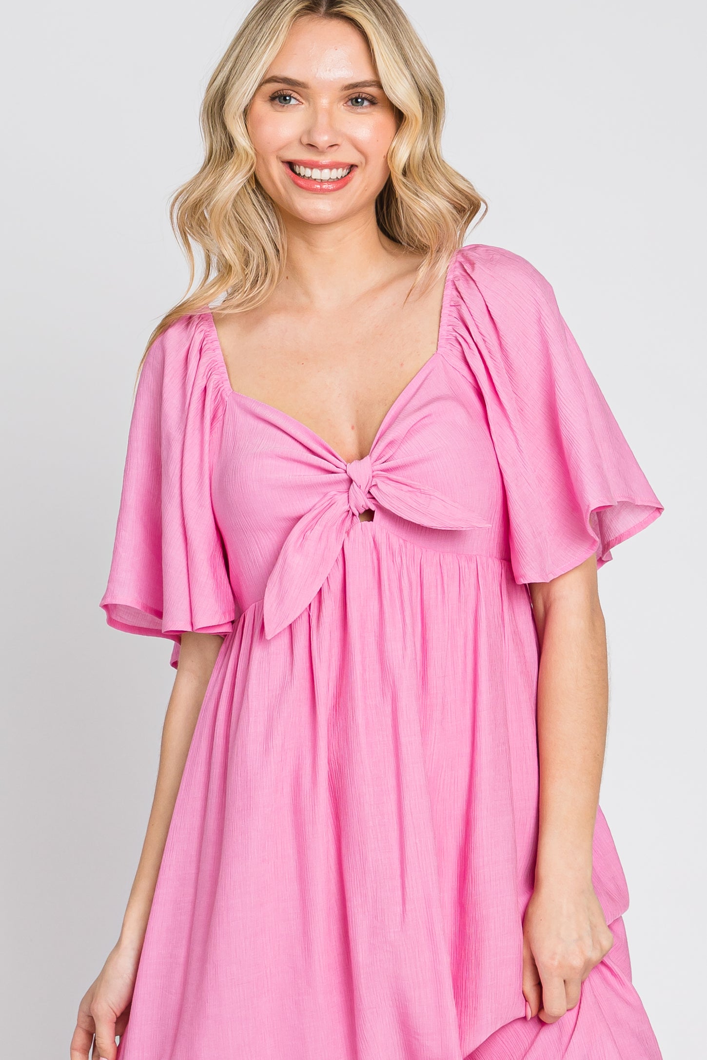 woman wearing a pink tie-front dress with flutter sleeves and a relaxed fit