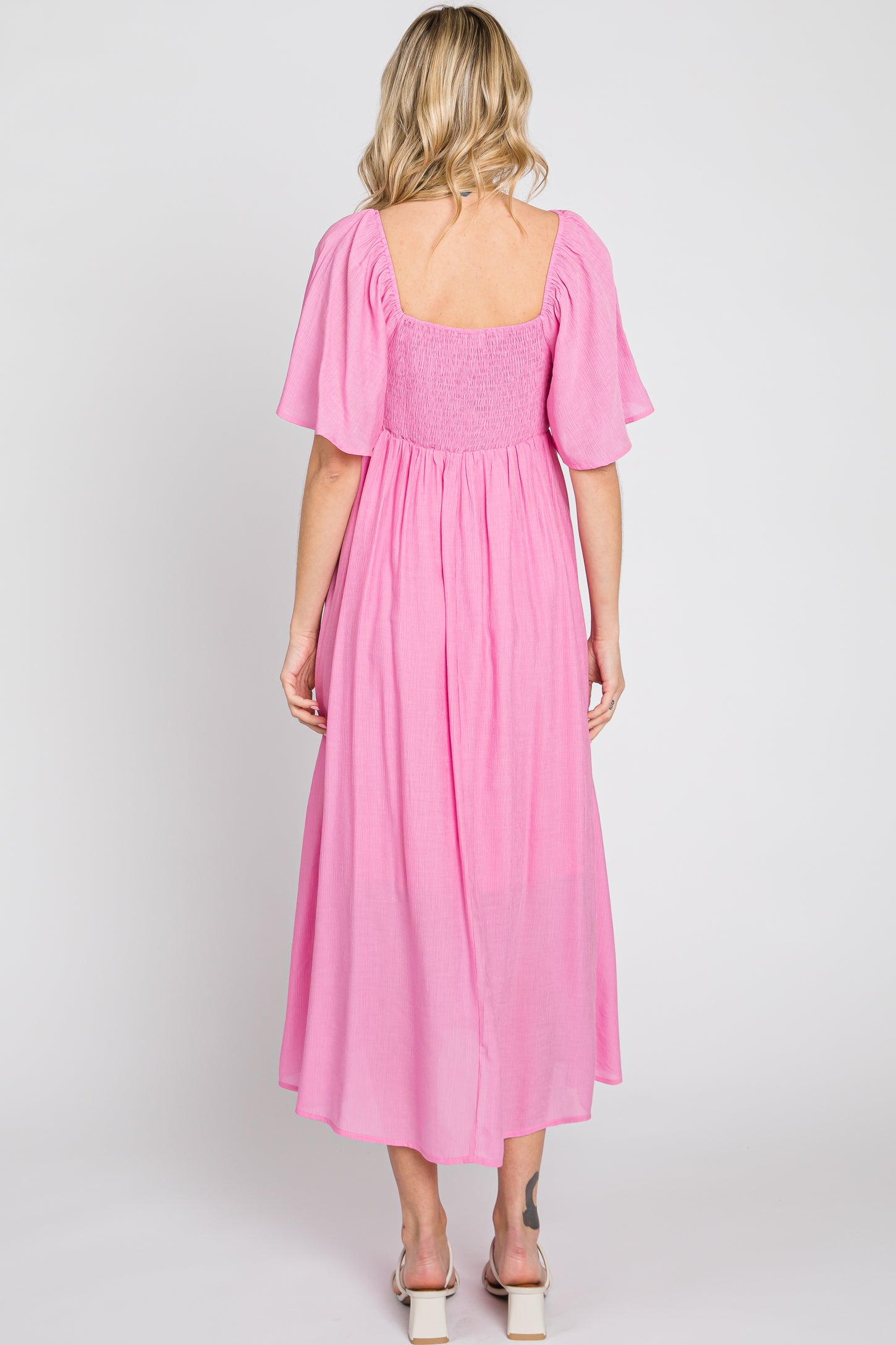 woman wearing a pink smocked back maxi dress with short flutter sleeves and a square neckline