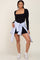 woman wearing a black long sleeve bodysuit and high-waisted shorts, styled with a blue and white striped shirt tied around her waist