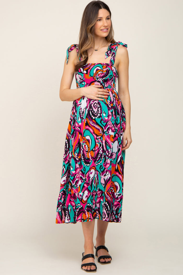 woman wearing a colorful patterned maternity maxi dress with adjustable tie straps and holding her baby bump