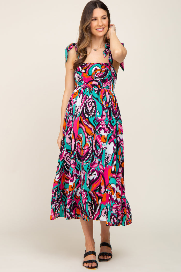 woman wearing a vibrant multi-colored maternity dress with tie straps and a flowing skirt, showcasing her baby bump