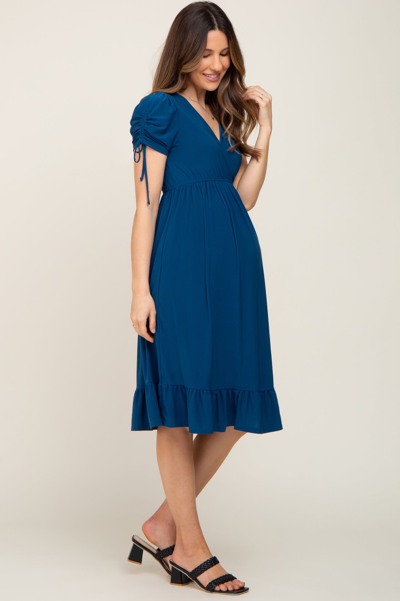 woman wearing a teal maternity dress with puff sleeves and a ruffle hem, showing her baby bump