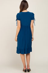 woman wearing a teal maternity dress with puff sleeves and a ruffled hem, seen from the back