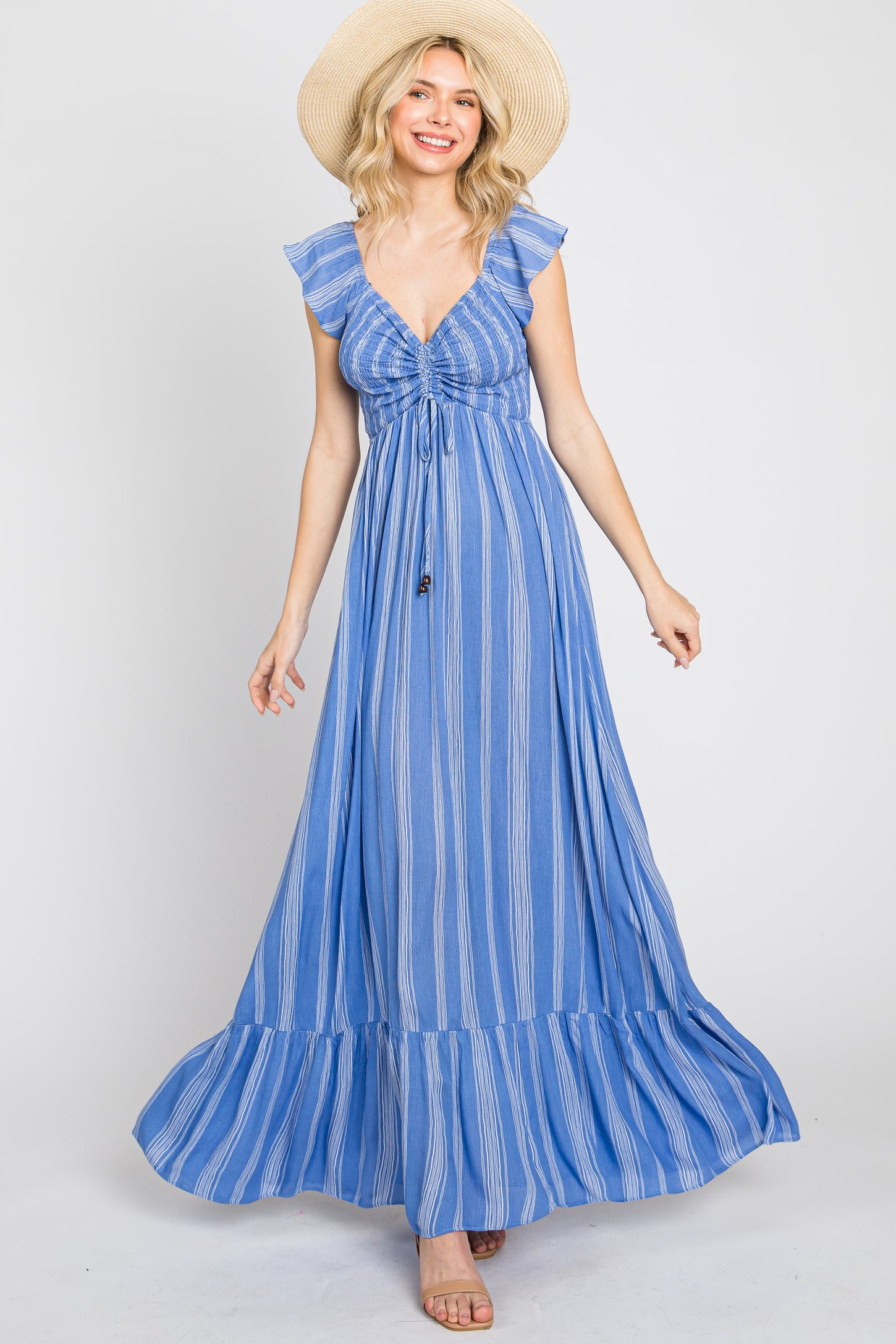 woman wearing a blue striped maxi dress with ruffle sleeves and a tied front, smiling while spinning in a sunhat