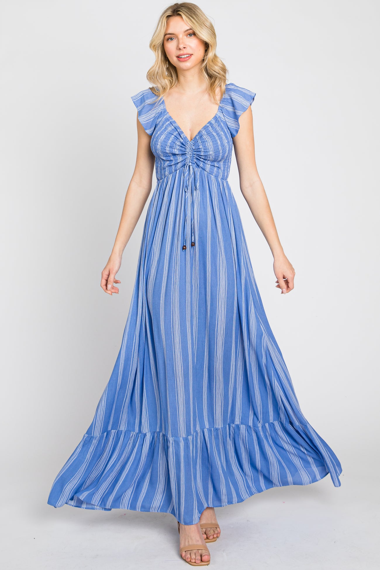 woman wearing a light blue striped maxi dress with ruffle sleeves and a tie front, standing and smiling