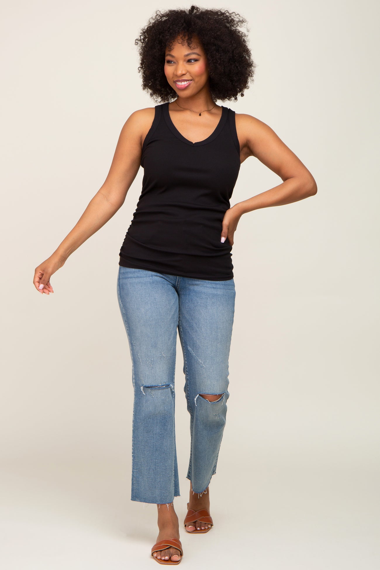 woman wearing a black sleeveless ribbed tank top and distressed light blue jeans, walking confidently