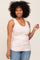 woman wearing a light pink ribbed tank top, smiling and standing against a neutral background