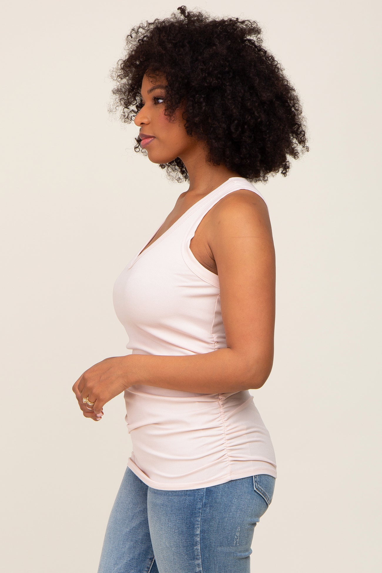 woman wearing a light pink sleeveless ribbed top with gathered detailing and paired with blue jeans
