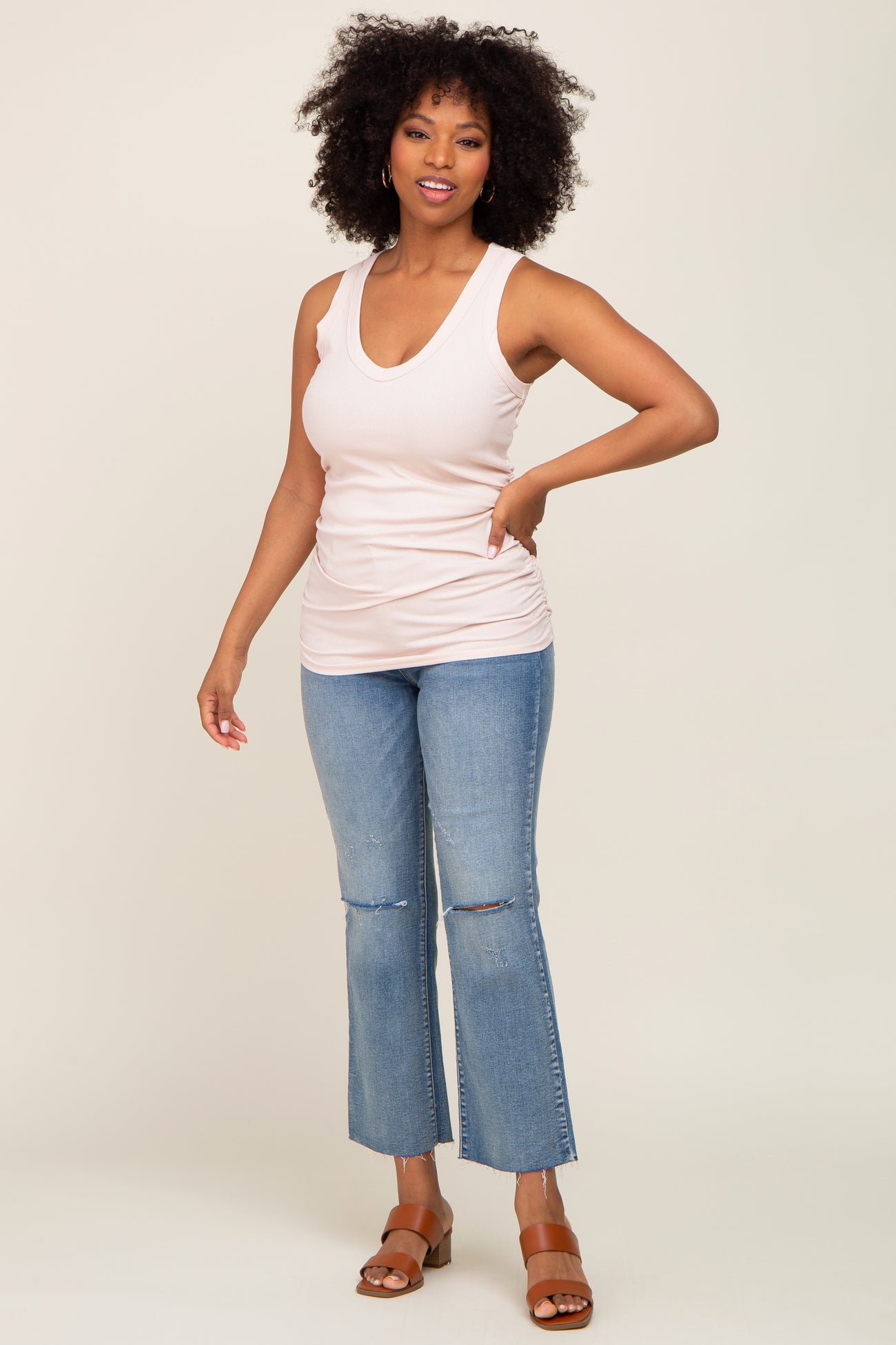 woman wearing a light pink sleeveless top and light blue flared jeans, standing and smiling.