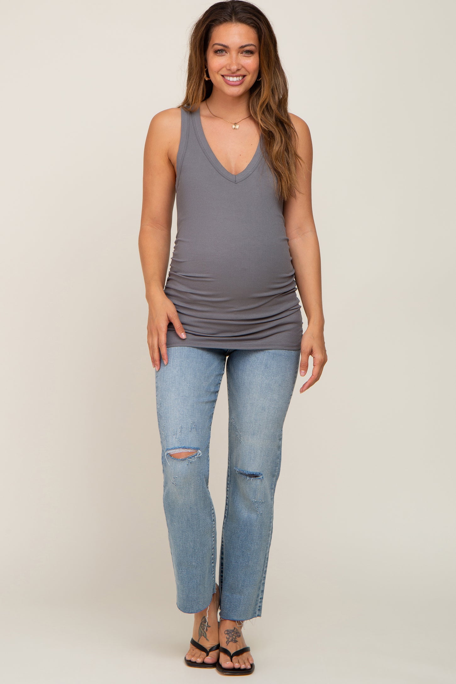 woman wearing a gray maternity tank top with a deep v-neck and distressed blue jeans, showing her baby bump