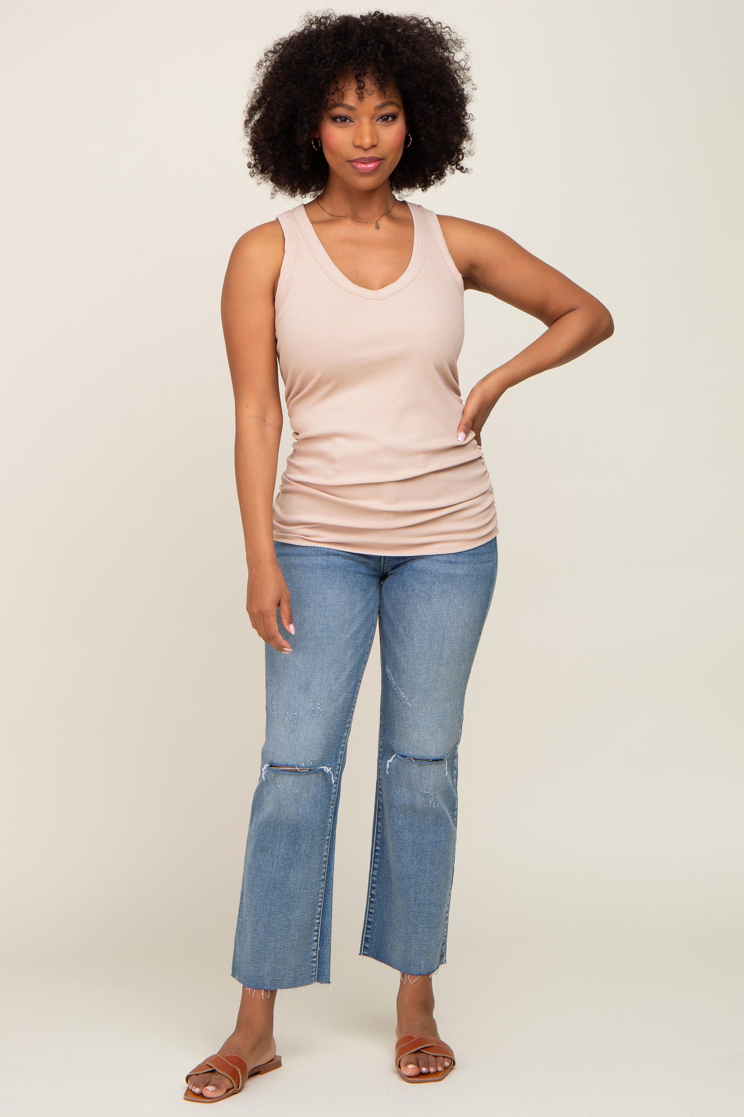 woman wearing a light beige ribbed tank top and distressed wide-leg jeans, styled with brown sandals