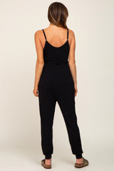 Back view of a woman wearing a black sleeveless maternity jumpsuit with spaghetti straps and cinched waist