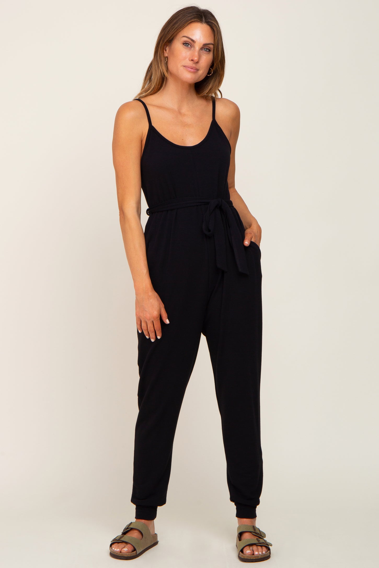 woman wearing a black spaghetti strap jumpsuit with a tie waist and side pockets