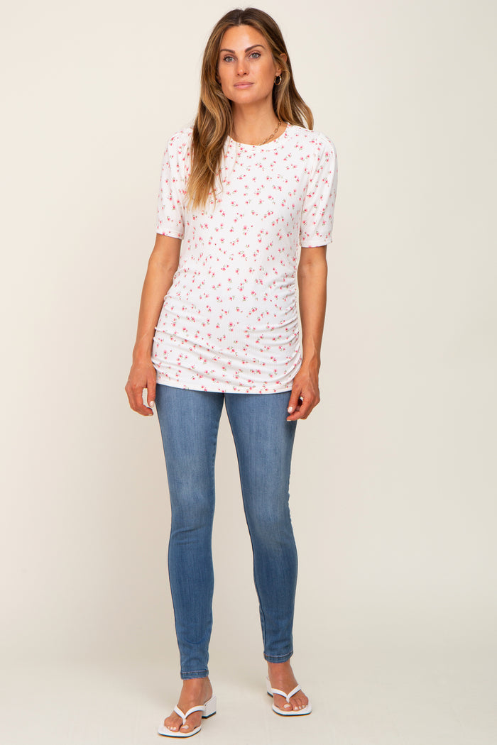 woman wearing a white short sleeve top with floral print and ruched sides paired with blue skinny jeans