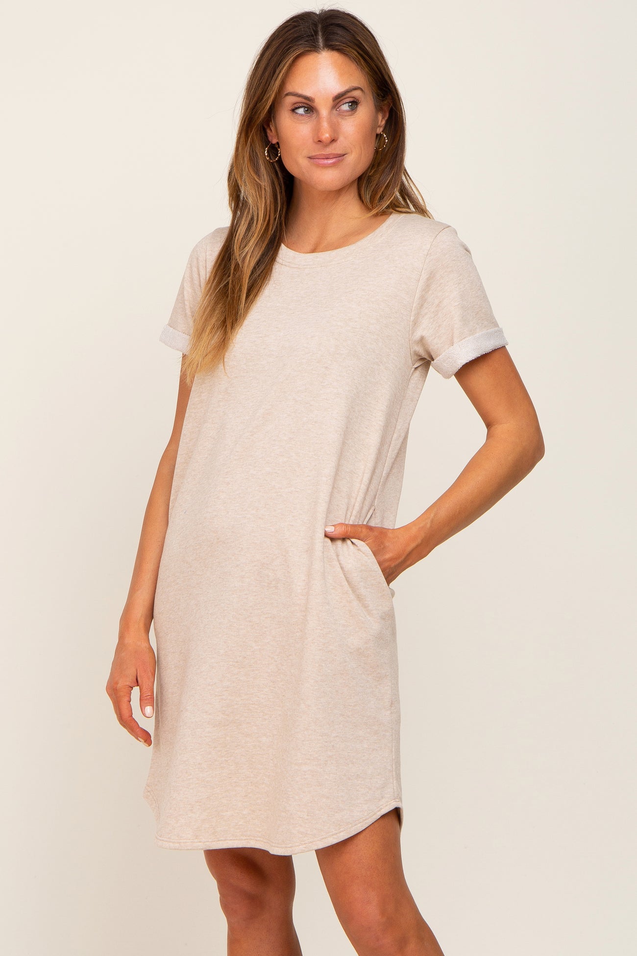 woman wearing a beige short sleeve t-shirt dress with rolled cuffs and side pockets