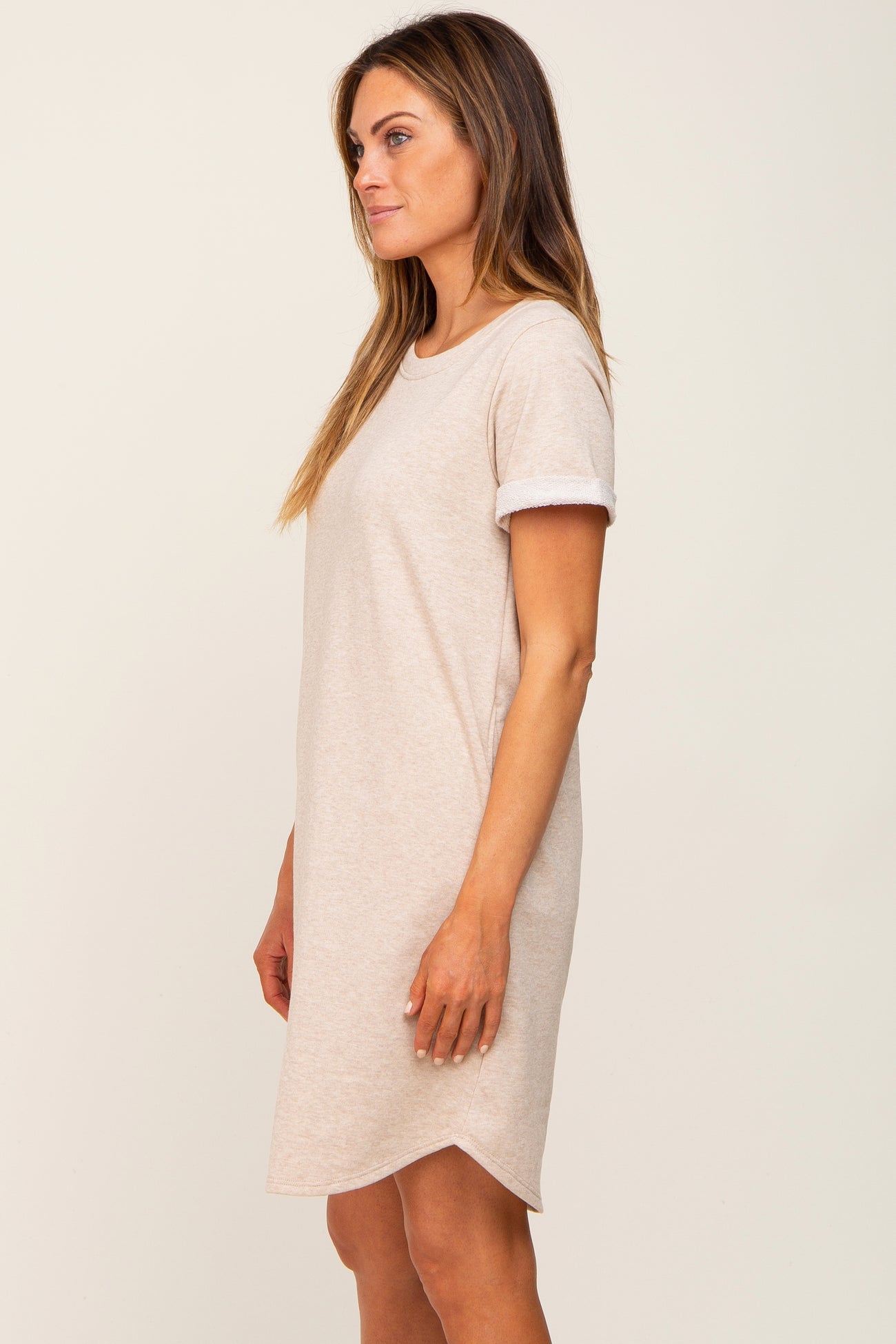 woman wearing a beige short sleeve t-shirt dress with rolled cuffs and a slightly curved hemline