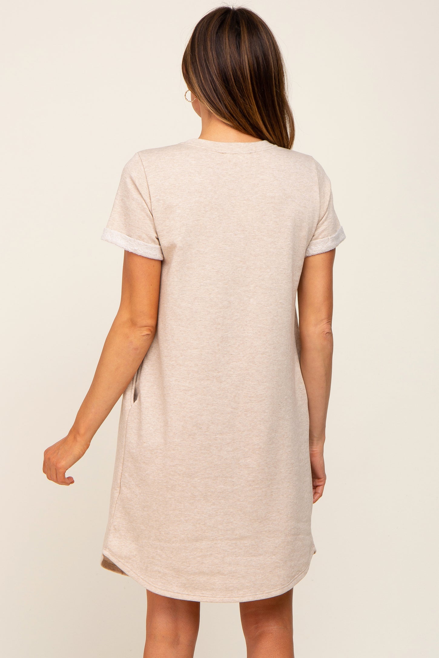 woman wearing a light beige short sleeve casual dress with rolled cuffs and a relaxed fit, viewed from the back