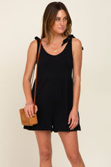 woman wearing a black sleeveless romper with tie-shoulder details and a brown woven crossbody bag