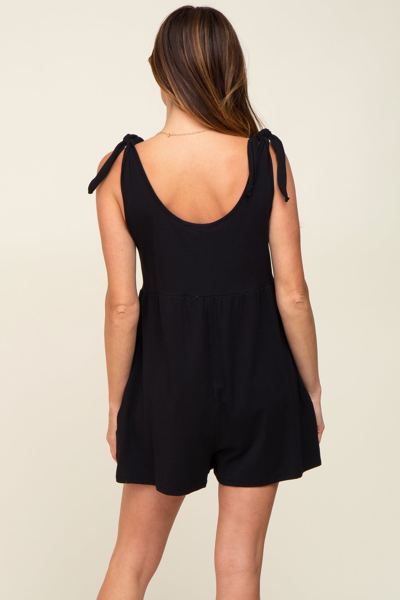 woman wearing a black romper with tie shoulder straps and a relaxed fit, showing the back view