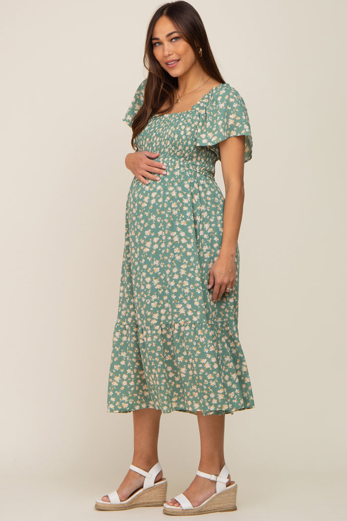 pregnant woman wearing a green floral smocked maternity midi dress and white wedge sandals