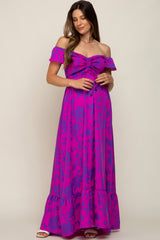 woman wearing a purple off-shoulder maternity maxi dress with gathered detailing and a flowy skirt, holding her baby bump