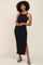 woman with afro hair wearing a black ribbed sleeveless midi dress with side slit and patterned heels