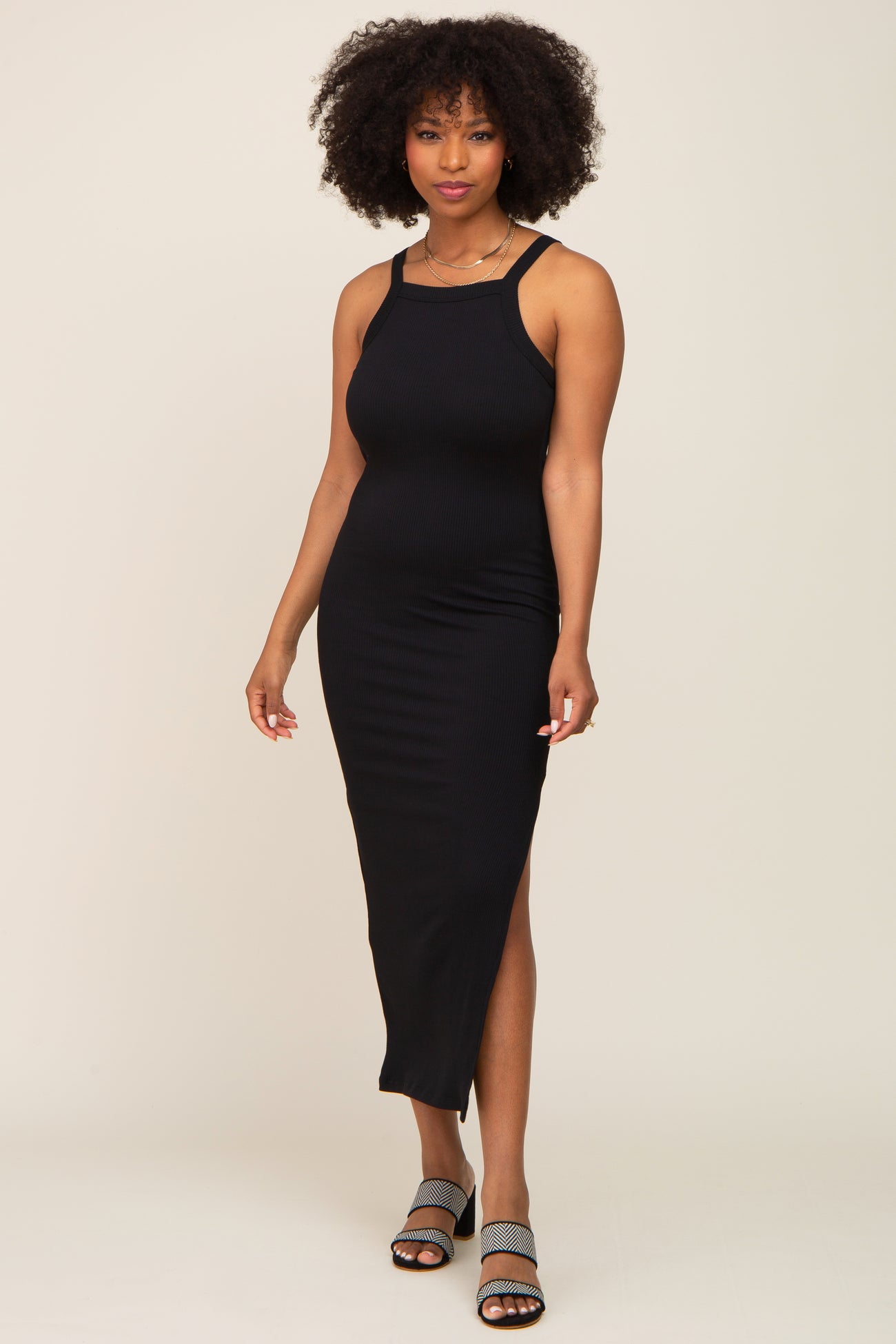 woman with afro hair wearing a black ribbed midi dress with side slit and patterned sandals