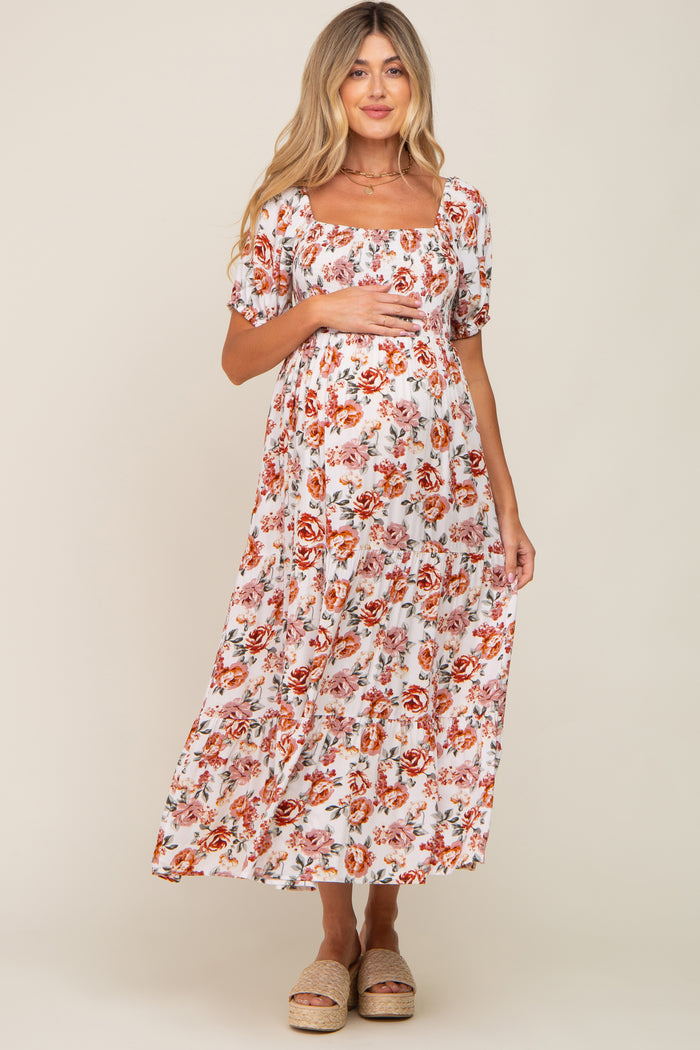 woman wearing a white floral maternity maxi dress with square neckline and puff sleeves, holding her baby bump