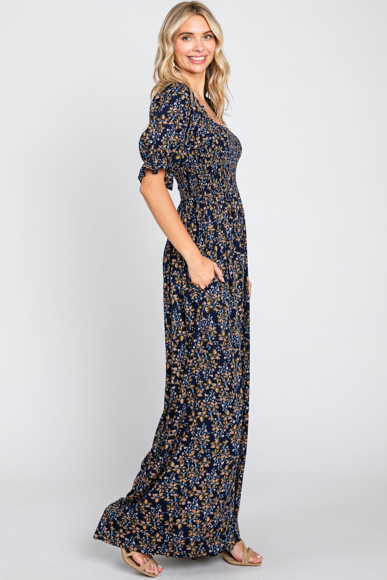 woman wearing a navy floral maxi dress with puff sleeves and pockets, standing sideways