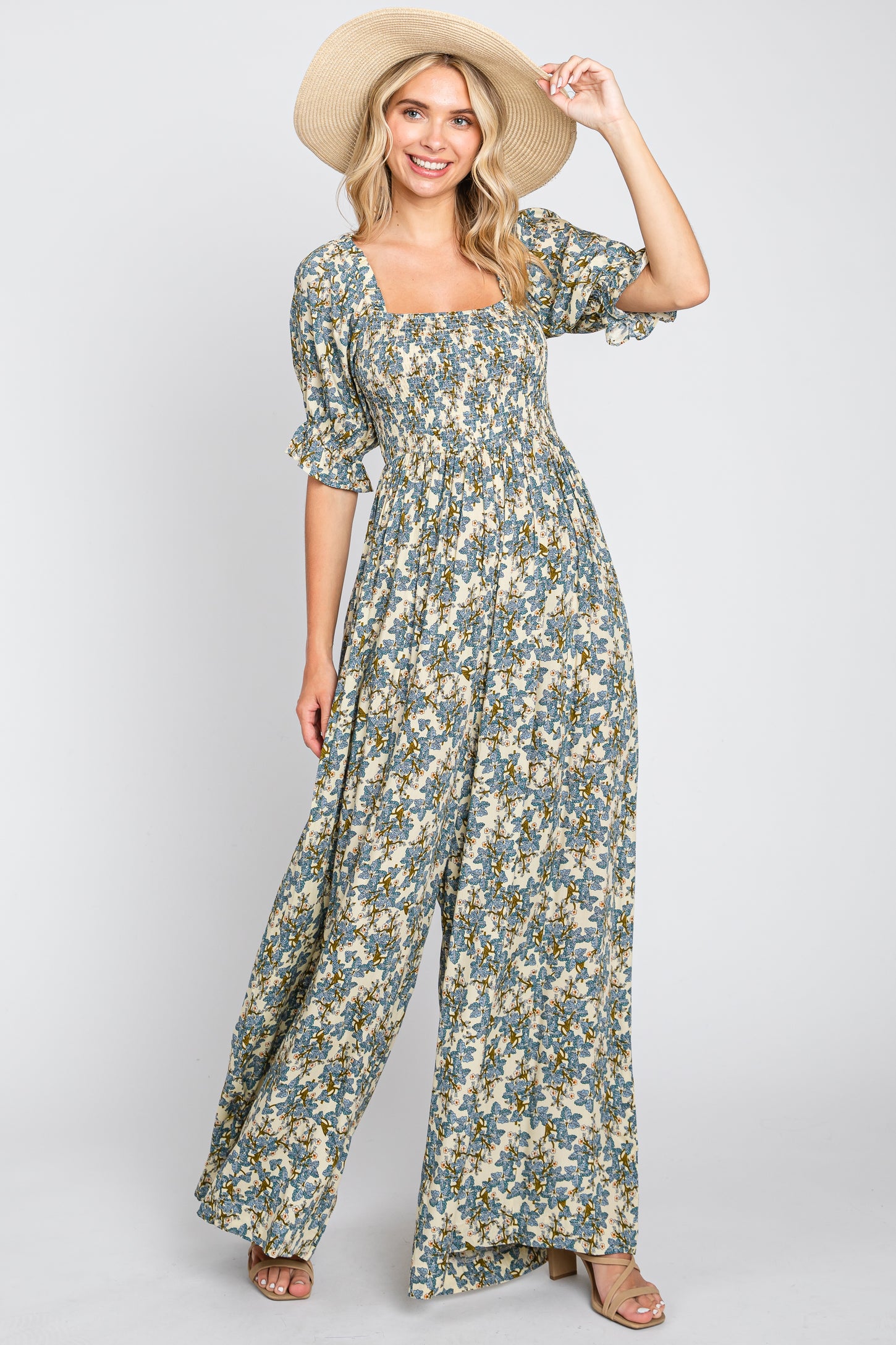 woman wearing a green floral maxi dress with puff sleeves and a square neckline, holding a straw hat
