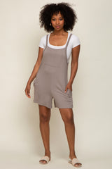 woman wearing a gray short overall dress with a white t-shirt underneath and standing in casual sandals