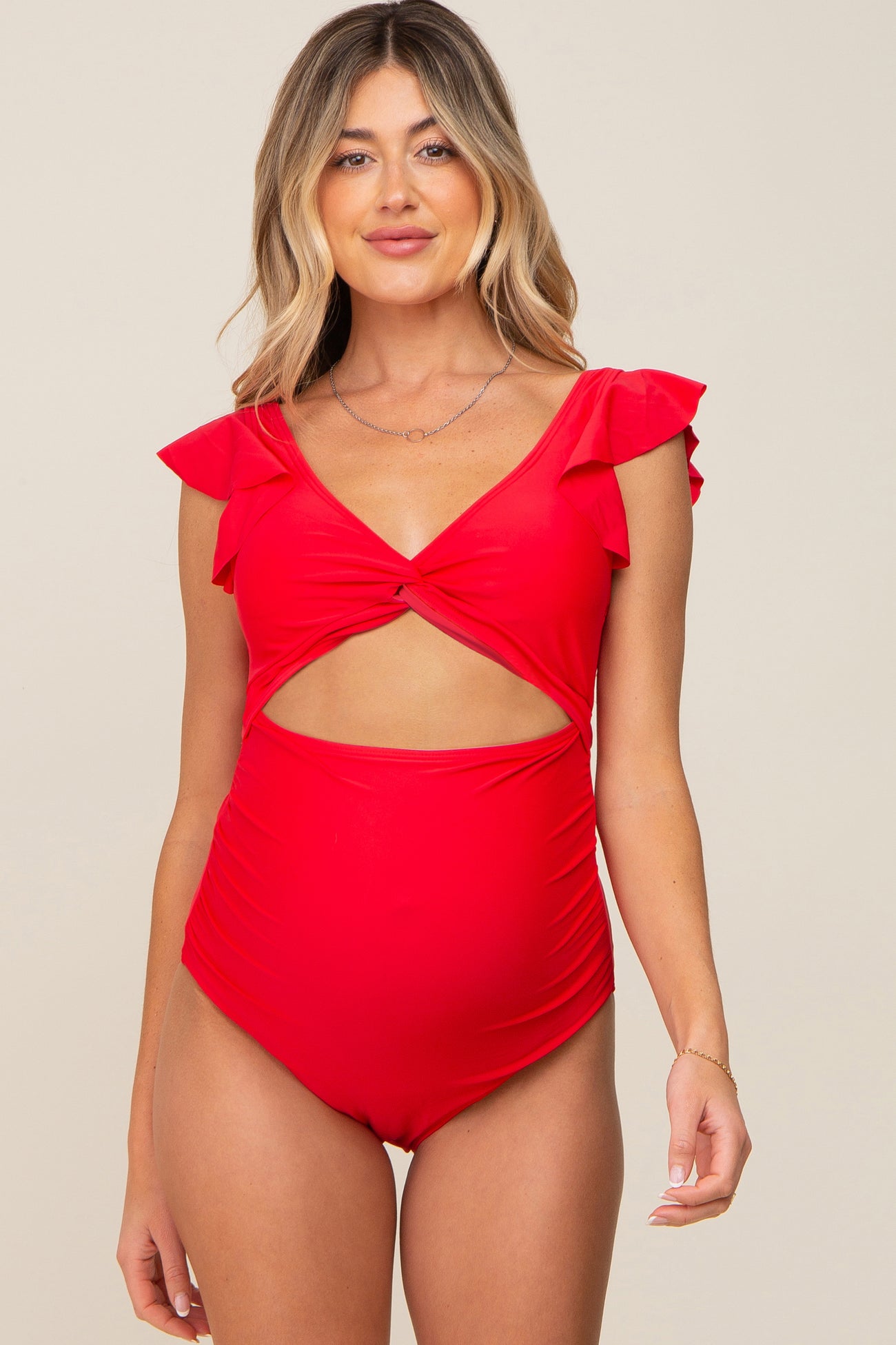 woman wearing a red maternity swimsuit with ruffle sleeves and a cutout design, showcasing her baby bump