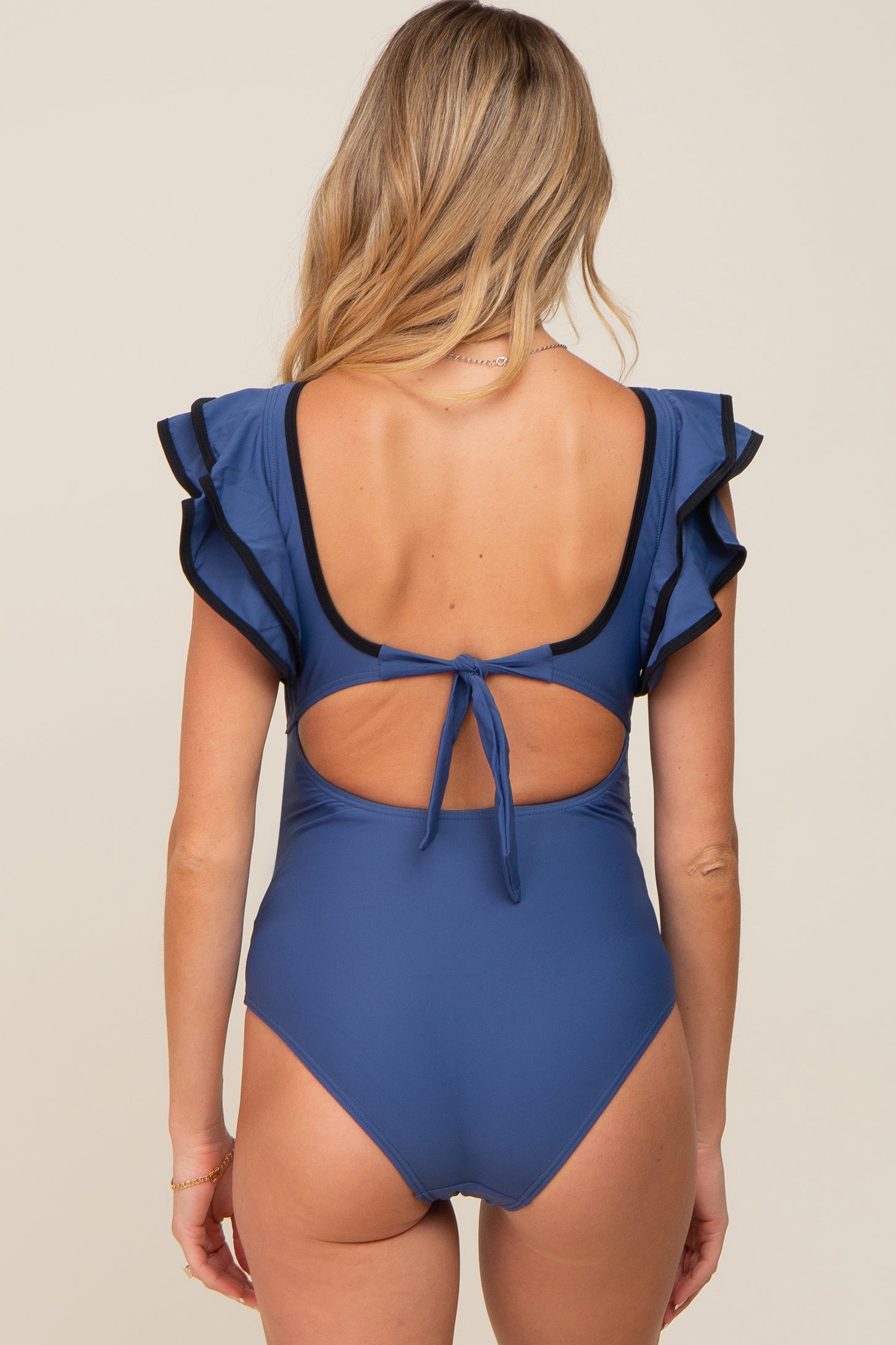woman wearing a navy blue maternity swimsuit with ruffled sleeves and a tie back detail
