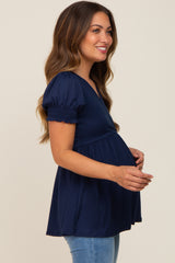 woman wearing a navy blue maternity top with short puff sleeves and a fitted waist, showing her baby bump