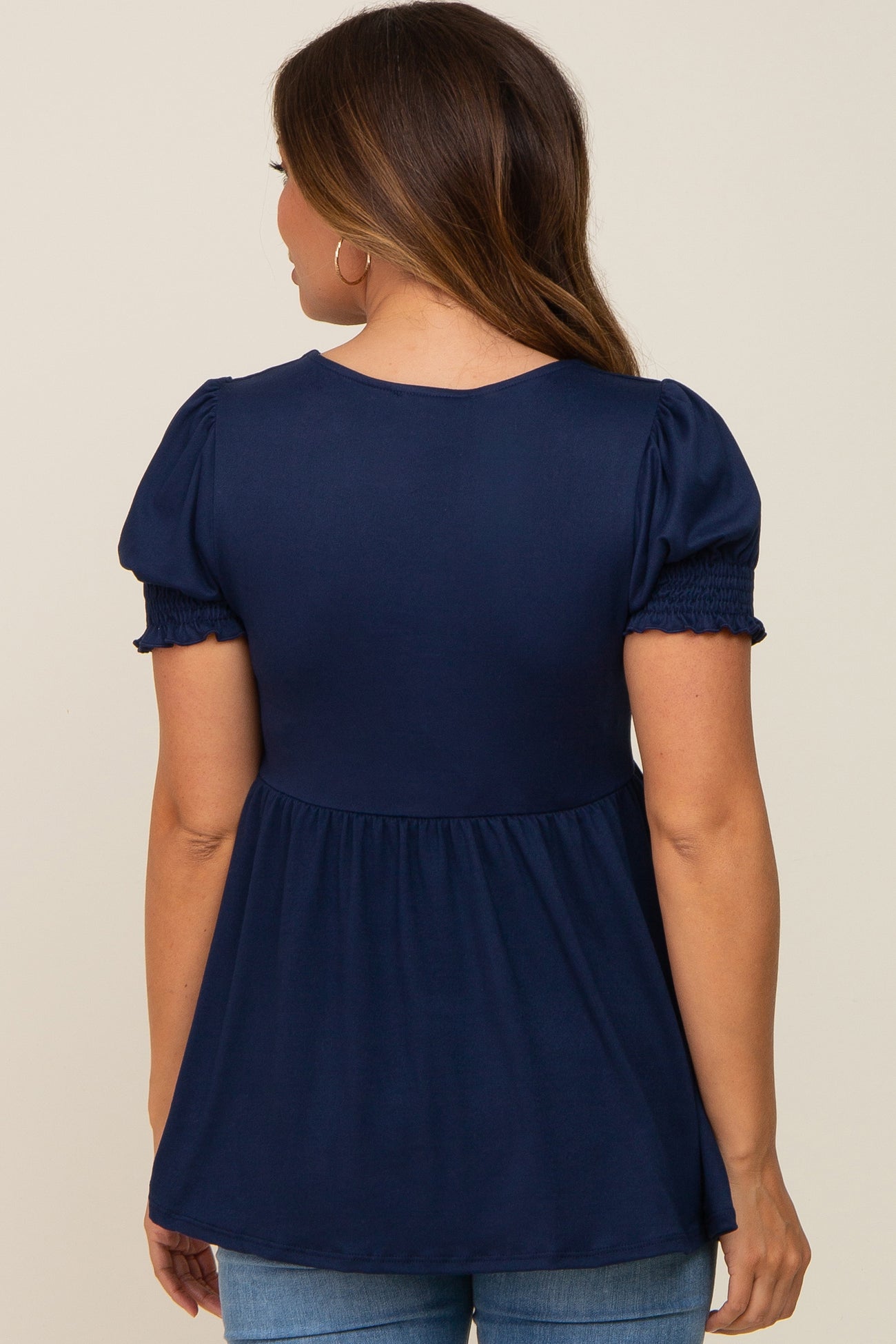 woman wearing a navy blue maternity top with puff sleeves and a gathered waist, showing her baby bump from the back