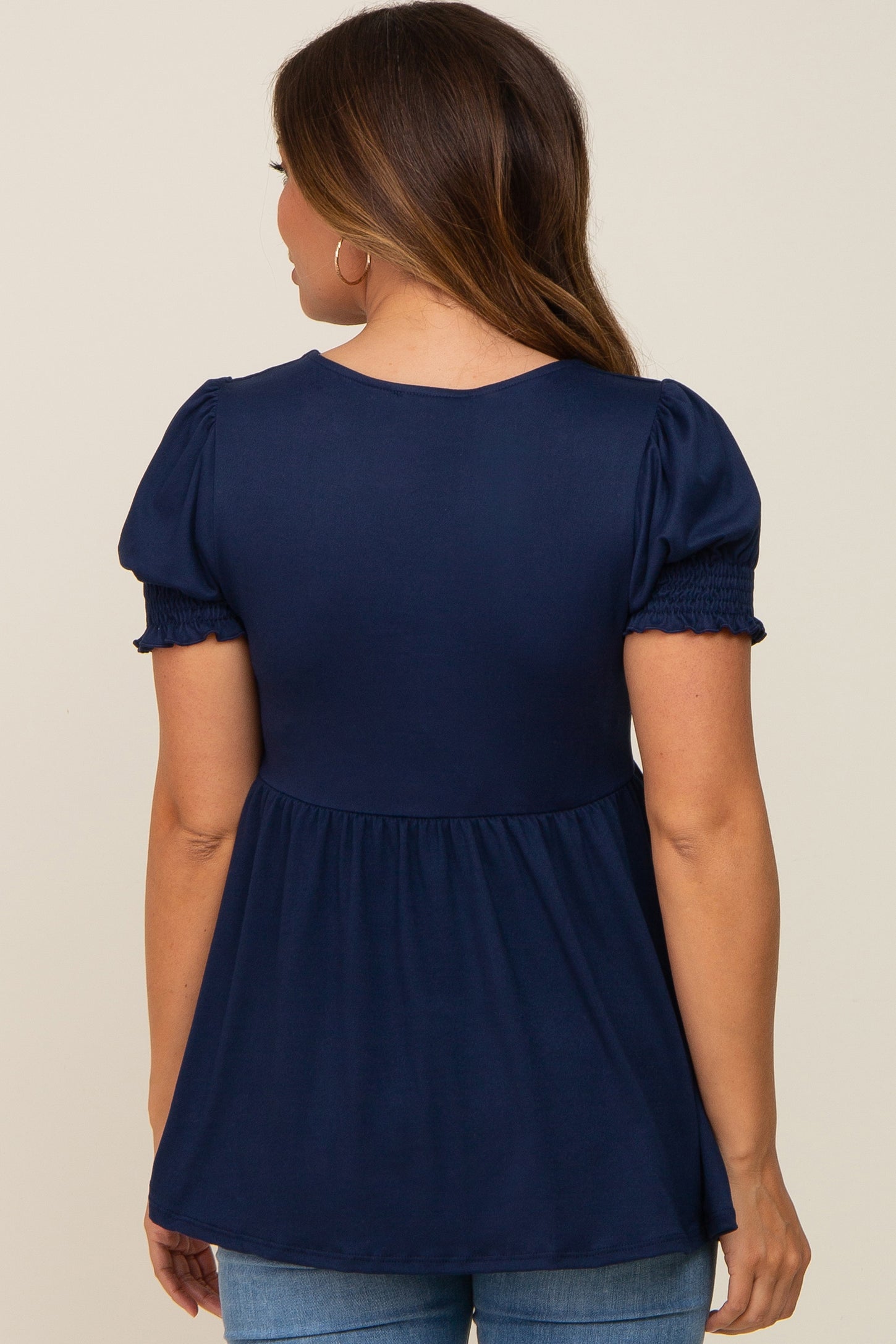 woman wearing a navy blue maternity top with puff sleeves and a gathered waist, showing her baby bump from the back