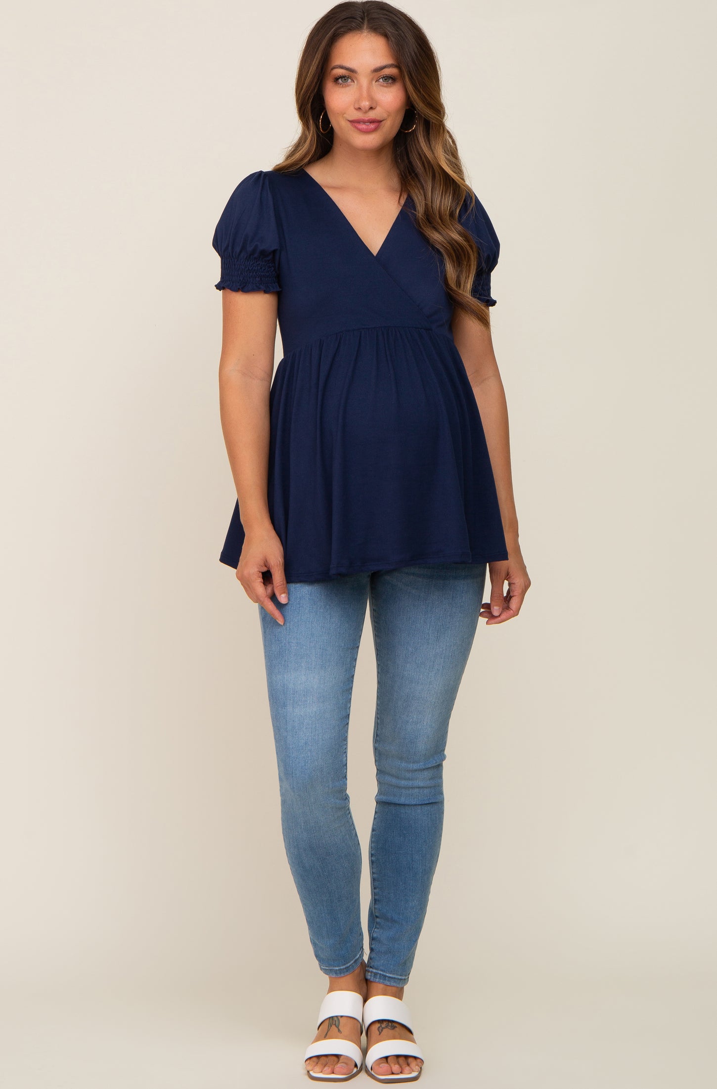 woman wearing a navy blue maternity top with puff sleeves and a fitted empire waist, paired with light blue skinny jeans