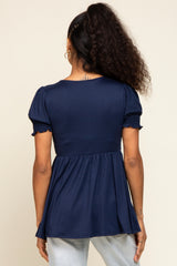 woman wearing a navy blue peplum top with short smocked sleeves, viewed from the back